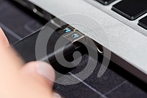 Hand inserting USB flash memory drive plugged into a computer laptop port.