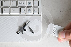 The hand inserts a compact SD card into the netbook slot, on which lie a miniature knife and a gun. The concept of computer games