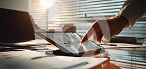 The hand interacting with a tablet displaying financial data in a modern office setting. AI generated image
