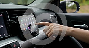 A hand is interacting with a touchscreen infotainment system inside a car, displaying
