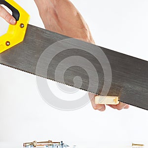 Hand of a joiner cutting wooden block with handsaw