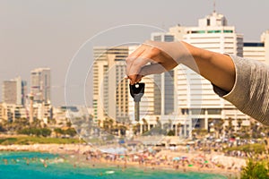 Hand with a key in the background of the sea with buildings and