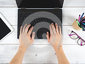 Hand on keypad of laptop with glasses and mobilephone on the table top view