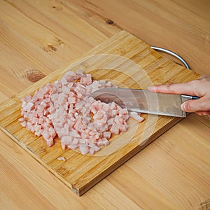 Hand with knife choping pieces of raw chicken meat