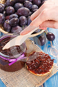 Hand with knife preparing fresh sandwiches with plum marmalade or jam, healthy sweet breakfast concept