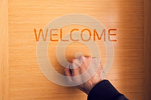 Hand knocking on door with welcome sign