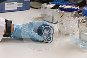 A hand of a lab technician with blue nitril gloves holding an timer in a science laboratory