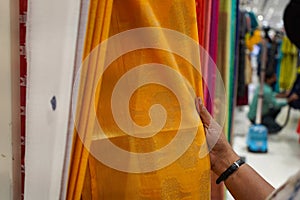 hand of a lady selecting yellow colored saree in a shop
