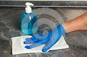 Hand in latex glove cleaning of kitchen table with paper towel and antiseptic liquid