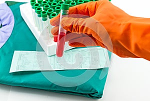 Hand with latex glove holding blood sample vial in front of blood test form and blue medical uniform