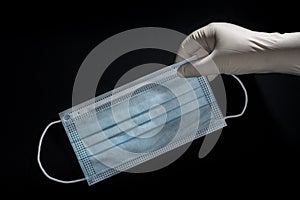 A hand with a latex glove picking up a face mask for virus protection on black background photo