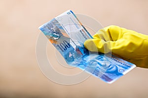 Hand with latex gloves giving a CHF banknote - world money concept