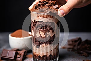 a hand layering brownie pieces on a chocolate shake