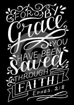 Hand lettering with bible verse For by grace you have been saved through faith on black background.