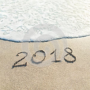 Hand lettering Happy New Year 2018 caption on sand of beach with