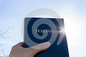 Hand Lifting Holy Bible to the Sky
