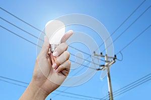 Hand with light bulb, electricity pole background