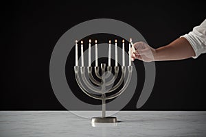 Hand Lighting Candle On Metal Hanukkah Menorah On Marble Surface Against Black Studio Background