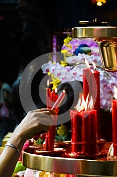Hand lighting red candle by altar in Buddhist temple, Taiwan, China. Religious symbols, spirituality concept, faith, God. Buddha.
