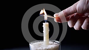 Hand Lights a Burnt Match on a Flame Burning Candle on a Black Background