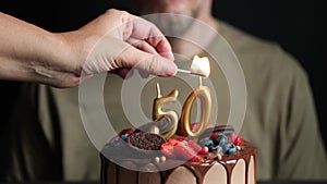 Hand lights candle on Birthday cake for 50 years anniversary. Fifty year old man makes wish. Slow Motion