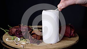 Hand Lights a White Candle against the Background of Rotating Dry Red Roses