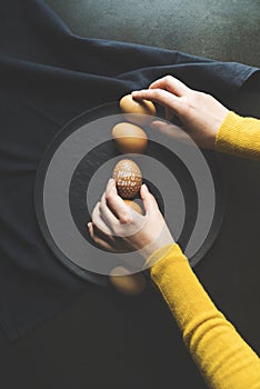 Hand lining up painted easter eggs in a row on black background, top view shot