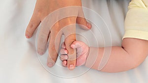 Hand of little baby and finger of adult on white sheet bed background