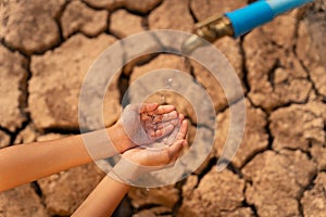 Hand of little girl wating for a drip of water from a faucet at dry ground. Water scarcity and crisis concept