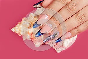 Hand with long artificial blue french manicured nails and a seashell