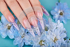 Hand with long artificial french manicured nails decorated with gemstones and blue flowers