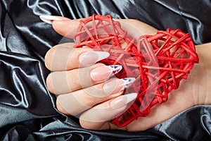 Hand with long artificial french manicured nails holding a heart