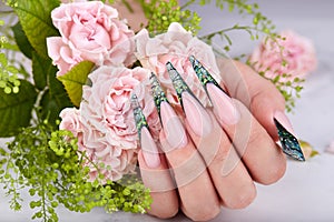 Hand with long artificial green french manicured nails decorated with rhinestones  and pink rose flowers