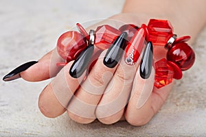 Hand with long artificial manicured nails colored with black and red nail polish