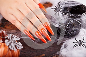 Hand with long artificial manicured nails colored with orange nail polish and Halloween decorations