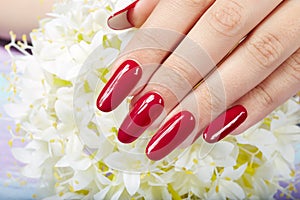 Hand with long artificial manicured nails colored with red nail polish