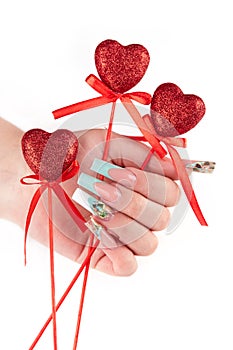 Hand with long artificial manicured nails colored with white and turquoise nail polish holding red hearts Valentine day decor