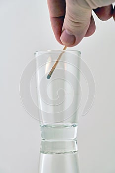 The hand lowers a lighted match into a transparent glass