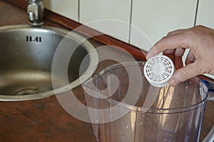 A hand lowers a silicon filter into an empty water jug