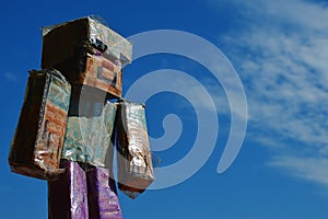 Hand made cardboard square shaped figure looking like Steve from Minecraft, smiling and sunbathing in summer sunshine.