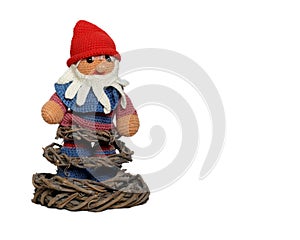 A hand made elf with red cap and beard standing on a stand made of tree roots. Gnome isolated