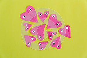 Hand made for Valentines day. Hand-painted pink paper hearts with eyes on a yellow background. Flat lay, cteative craft concept