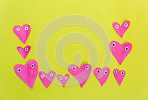 Hand made for Valentines or Mothers day. Hand-painted pink paper hearts with eyes on a yellow background. Flat lay, cteative craft