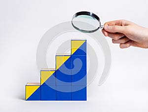 Hand with magnifier over career ladder from cubes. Study of professional development and growth perspectives