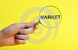 Hand with magnifier with word market on yellow background. Conducting research about new product, service, customers