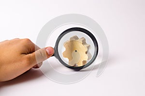 Hand with the magnifying glass is aimed at the wooden wheel gear. concept of studying the technological process and industry photo