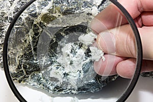 Hand with magnifying glass examines asbestos fibers