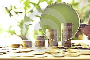 Hand with magnifying glass and money coins stack growing