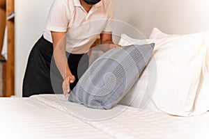 Hand of maid setting up pillow on bed sheet in hotel room