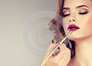 Hand of make-up master, painting lips of model. photo